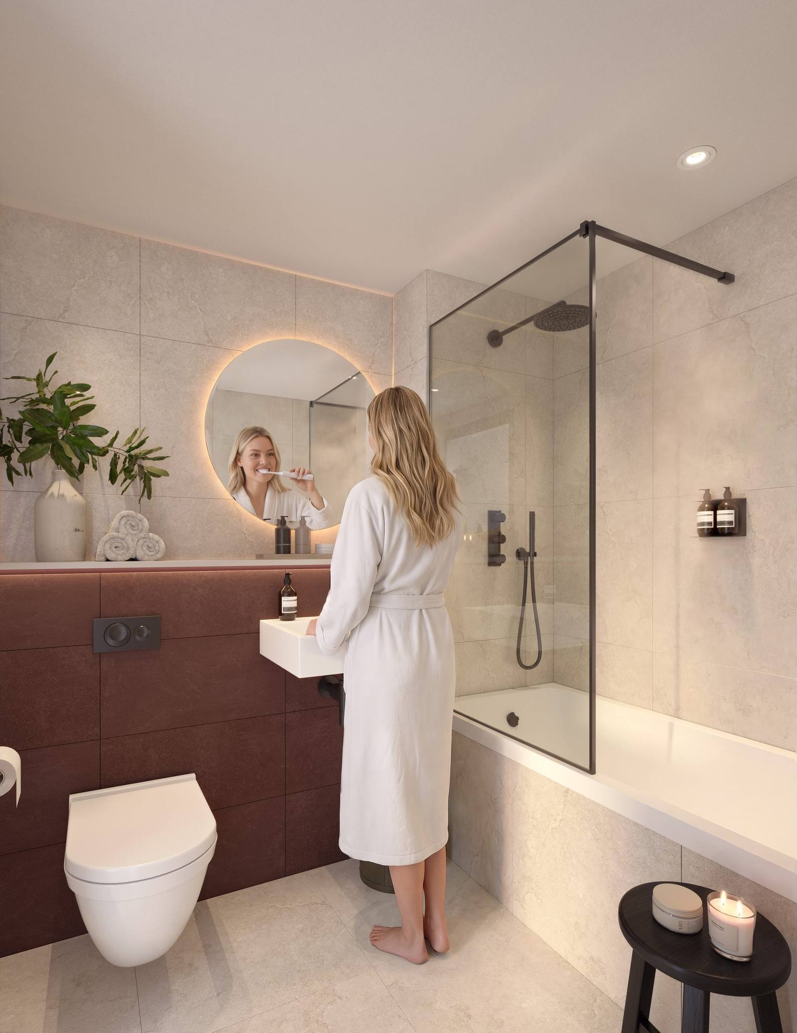 A bathroom with a walk-in shower and round lit mirror, with a woman in a white robe at the basin